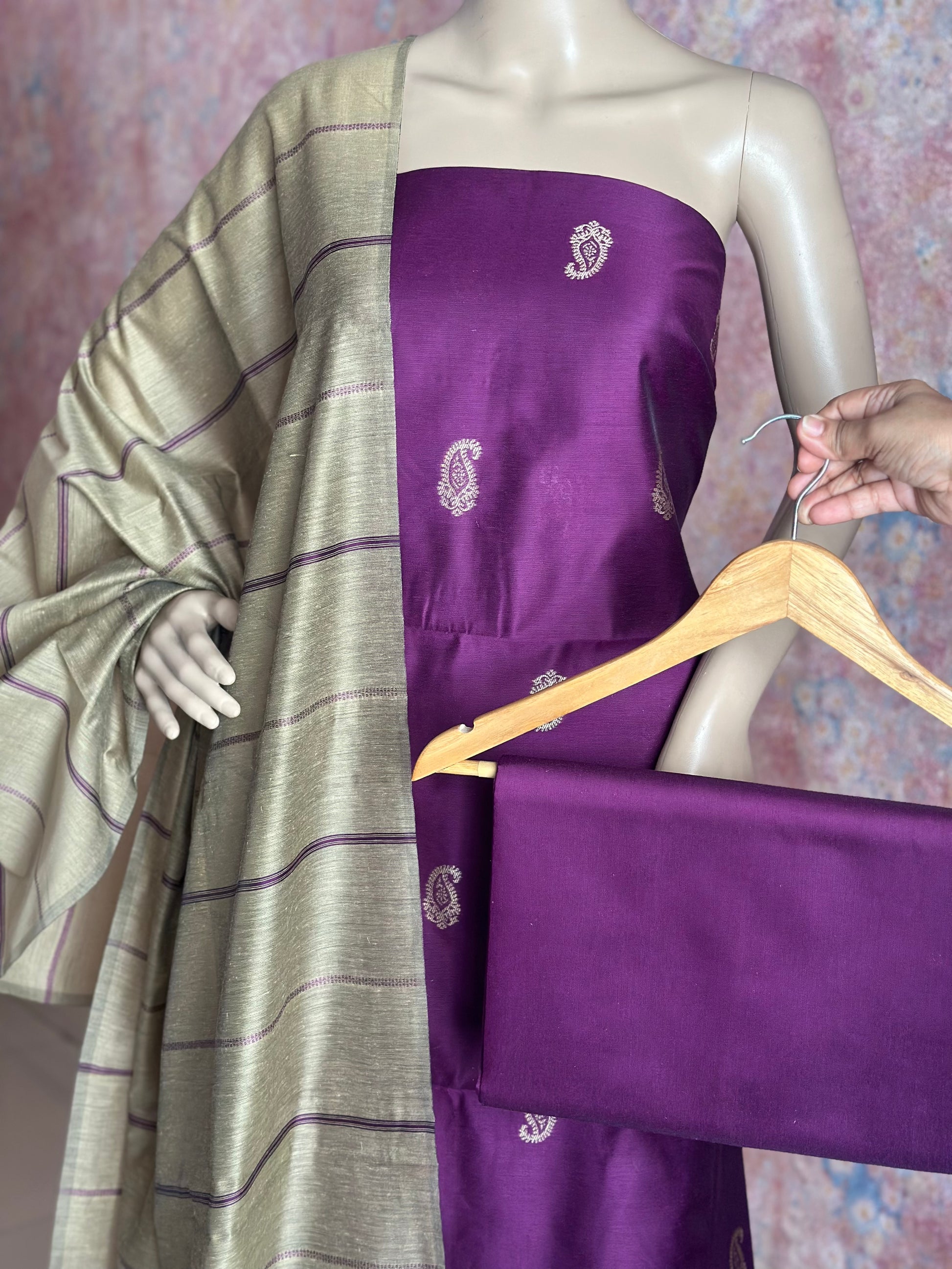 Purple unstitched suit set showing paisley top, striped dupatta and plain purple bottom fabric on a hanger.