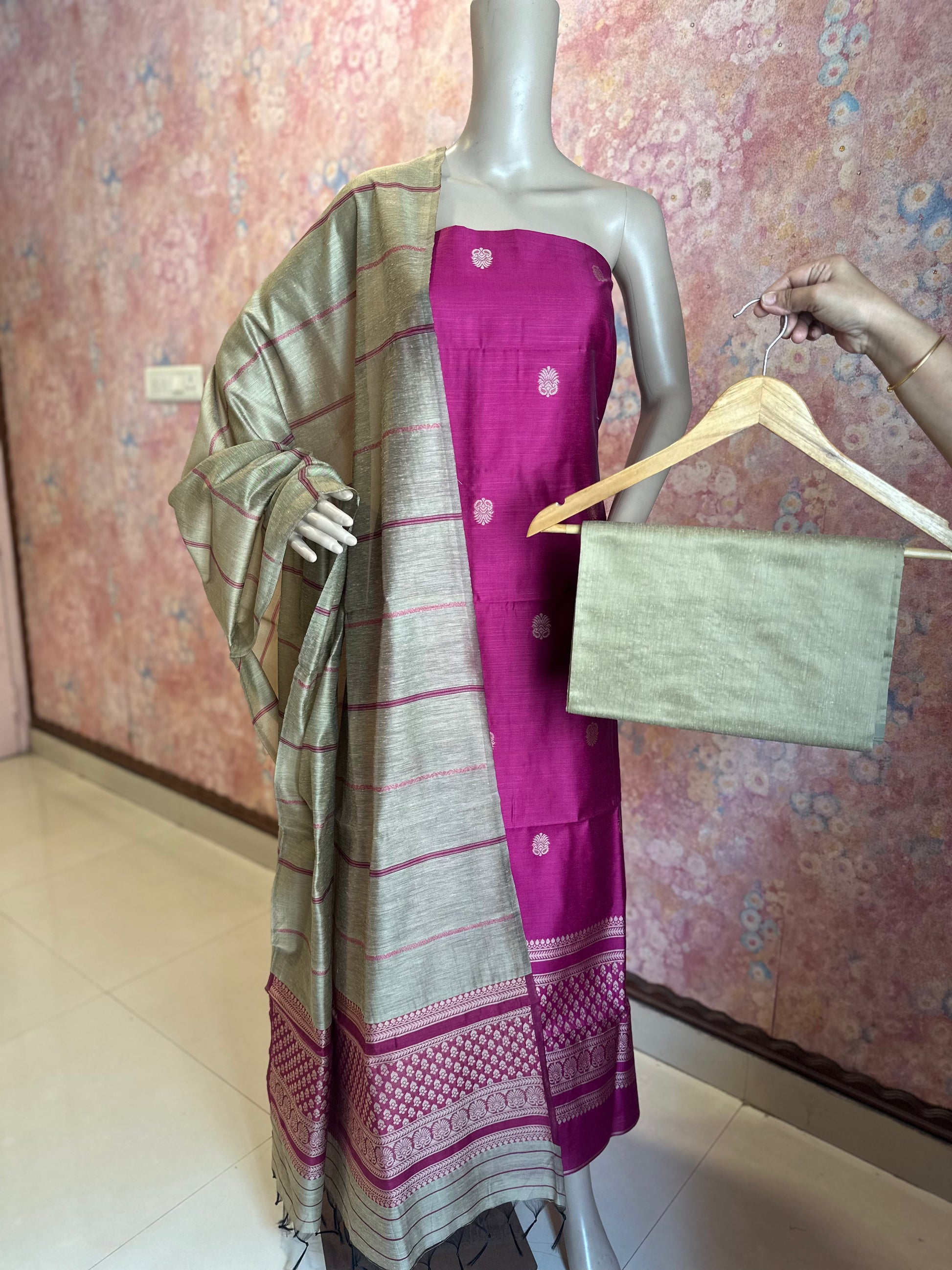 Dark Pink unstitched suit set with patterned top, contrasting striped dupatta and plain bottom fabric on a hanger.